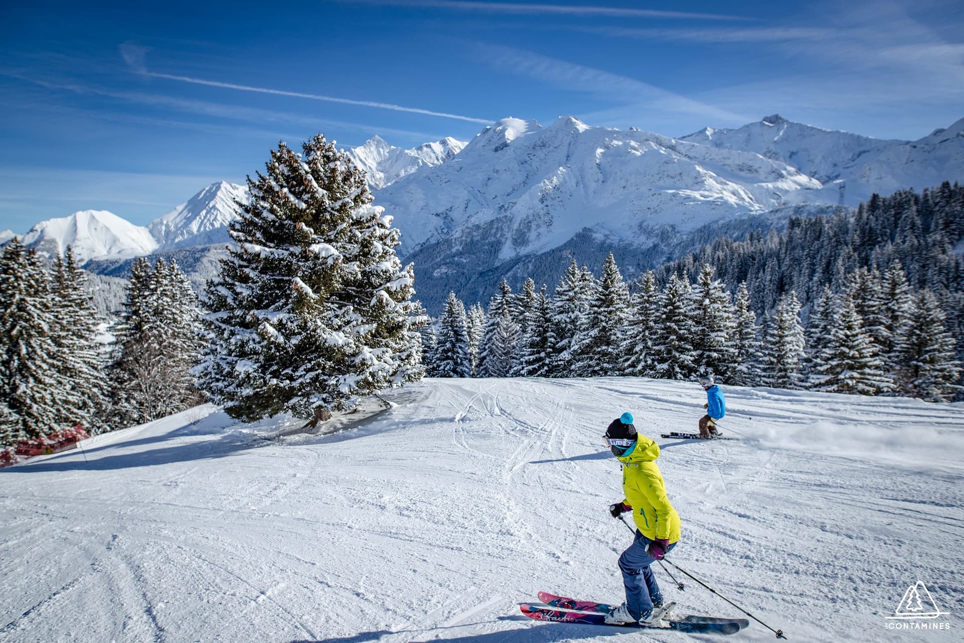 Two skiiers skiing down tree-lined ski slope in france